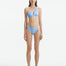 Model wearing the Eyre Baby Blue Bikini Bottom, highlighting the mid-rise design and shell-shaped gold button details.