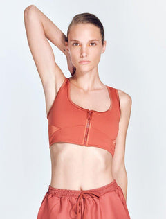 "Fanny Red Ochre Sports Bra front view featuring a square neck, satin matte contrast, and a front zip detail. "