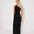 Front View: Model in Fewa Black Dress - MOEVA Luxury Swimwear, One Shouldered Ready to Wear Dress, Gold Sculpted Hoop Accessory, Side Slit, MOEVA Luxury Swimwear