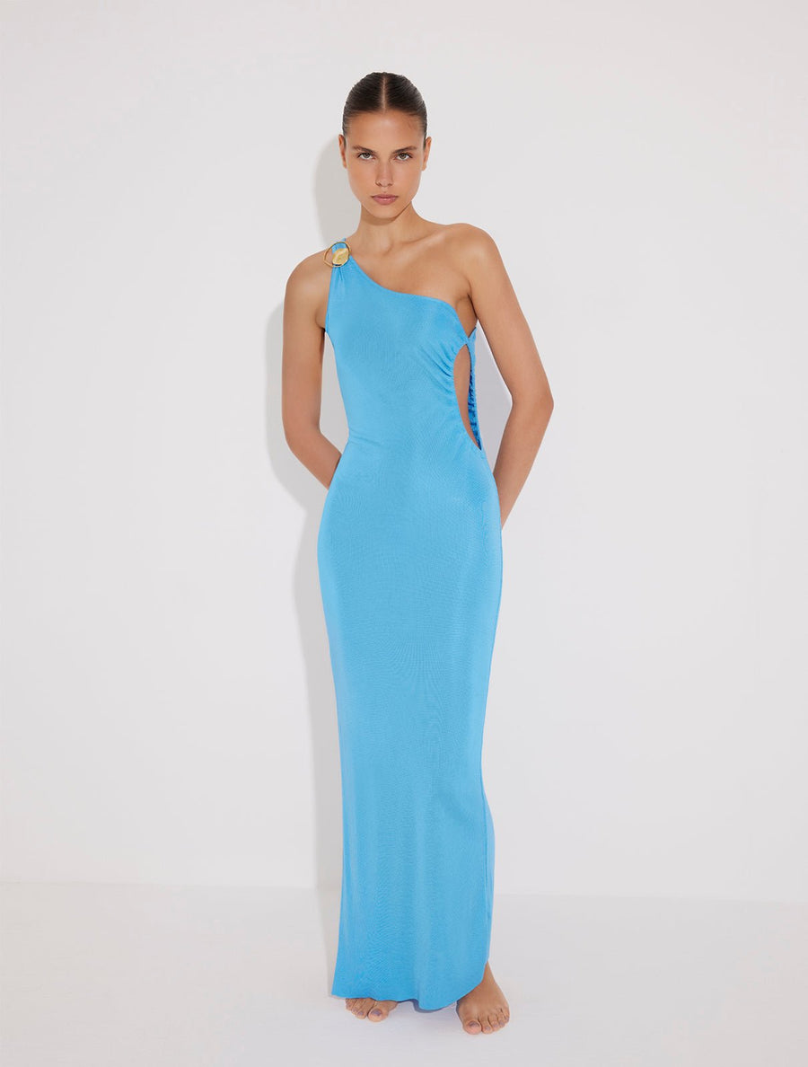 Front View: Model in Fewa Blue Dress - MOEVA Luxury Swimwear, One Shouldered Ready to Wear Dress, Gold Sculpted Hoop Accessory, Side Slit, MOEVA Luxury Swimwear