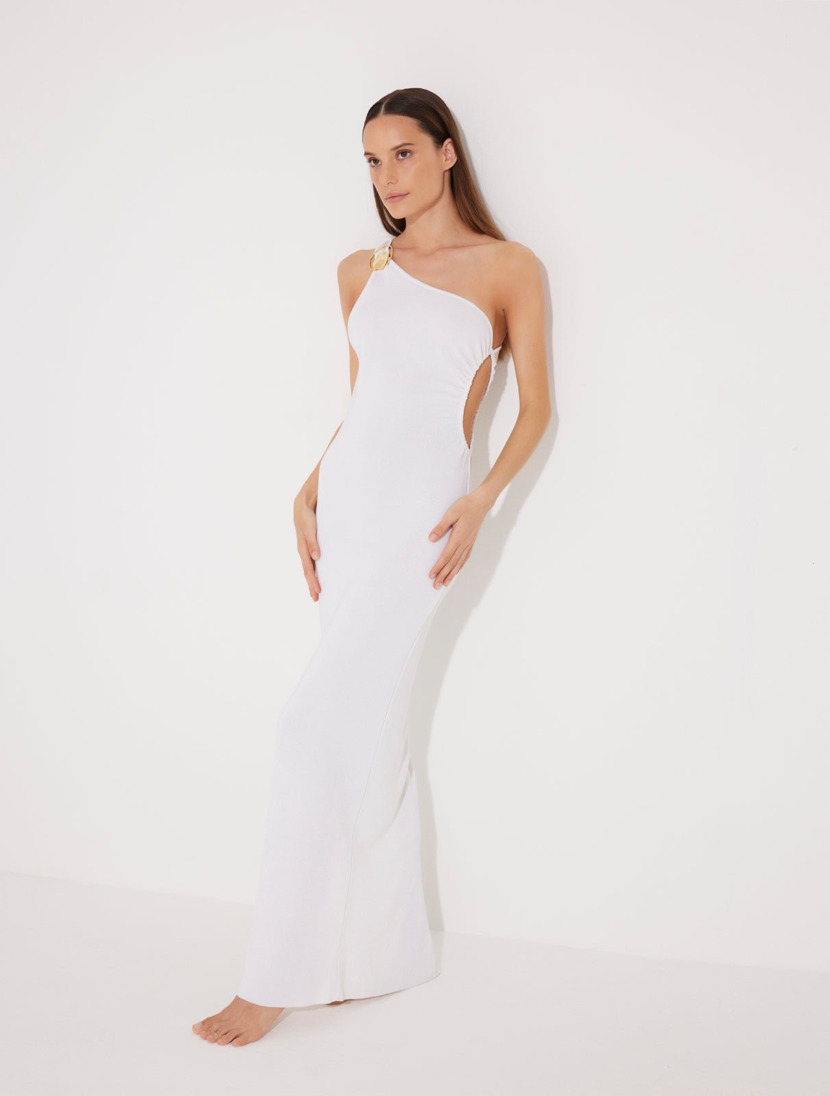 Front View: Model in Fewa White Dress - MOEVA Luxury Swimwear, One Shouldered Ready to Wear Dress, Gold Sculpted Hoop Accessory, Side Slit, MOEVA Luxury Swimwear