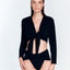 Front View: Model in Greta Shiny Black Shirt - MOEVA Luxury Swimwear, Cropped Silhouette, Made of Swimwear Fabric, Tie at the Front, Unlined, Comfort and Day to Night, MOEVA Luxury Swimwear