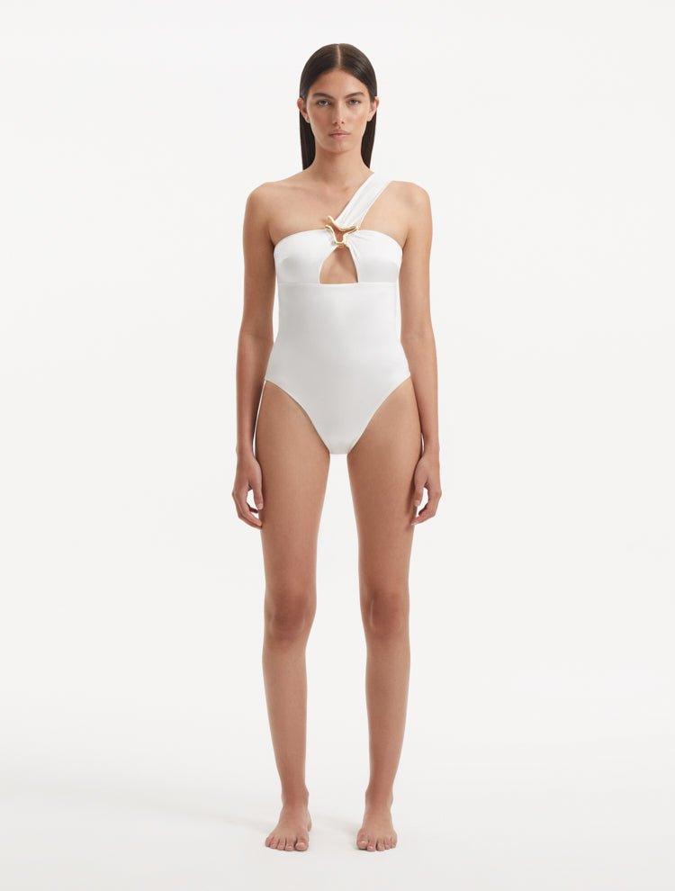 Model showcasing the Halin White Swimsuit, emphasizing the one-shoulder design and luxurious gold sculpted accessory.