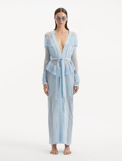 "Model wearing the Itzel baby blue kaftan from the front, showcasing its hand-knit design, translucent open knit, and dynamic fringe details, paired with a playful beach ensemble."
