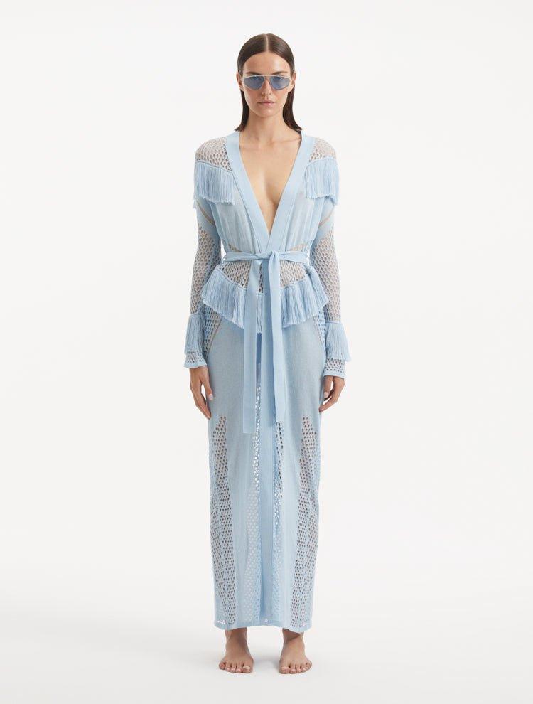 "Model wearing the Itzel baby blue kaftan from the front, showcasing its hand-knit design, translucent open knit, and dynamic fringe details, paired with a playful beach ensemble."