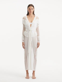 "Model showcasing the Itzel white kaftan from the front, highlighting its intricate hand-knit design, delicate fringes, and the subtle peek of a swimsuit underneath."