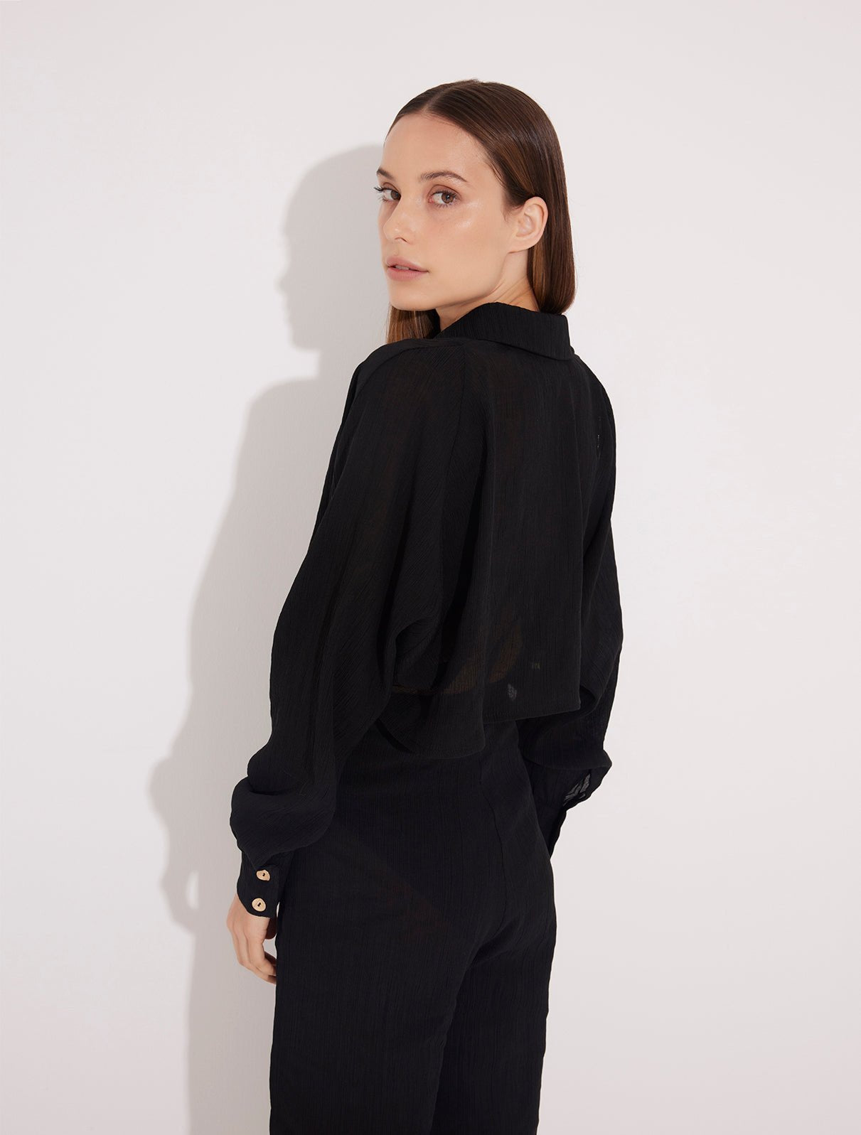 Back View: Model in Jacinta Black Shirt - MOEVA Luxury Swimwear, Gold Button Detail Throughout, Recycled and Textured Fabric, MOEVA Luxury Swimwear
