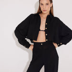 Front View: Model in Jacinta Black Shirt - MOEVA Luxury Swimwear, Cropped Shirt, Button Fastening Through Front, Soft Touch Fabric, Recycle Fabric MOEVA Luxury Swimwear