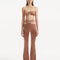 "Model wearing Jenna Brown Pants from the front, showcasing the high-waist, ankle-length design, flared slim fit, and intricate cut-out details."