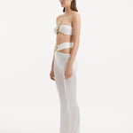 "Side view of the Jenna White Pants showcasing the elegant ankle-length cut, flared design, and the refined gold sculpted accessory at the waistband."