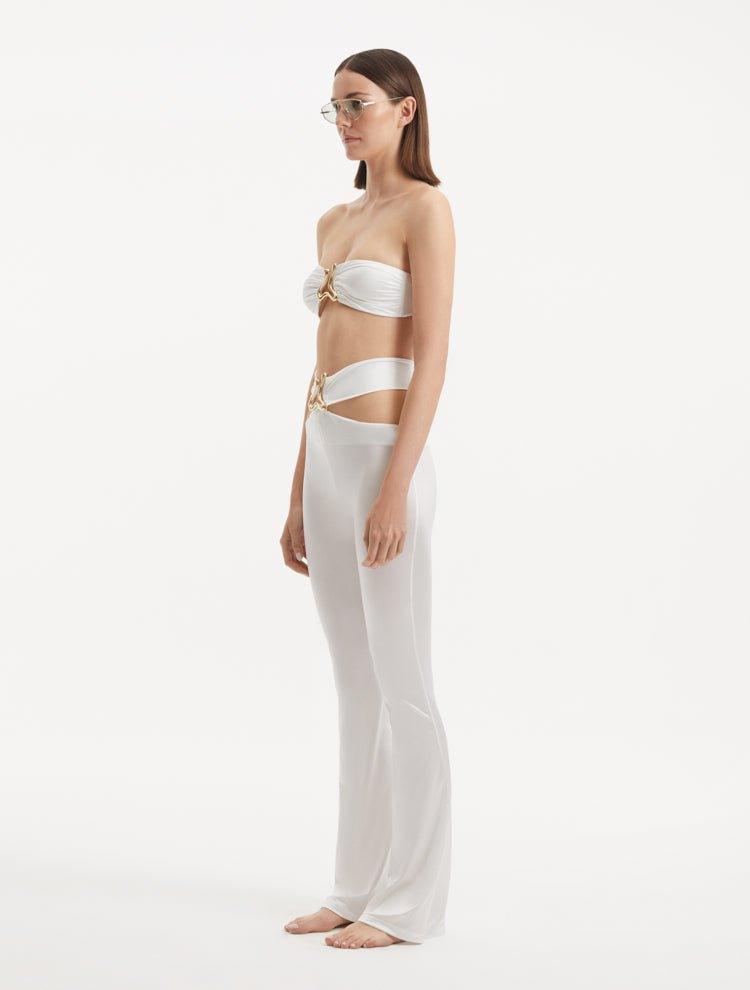 "Side view of the Jenna White Pants showcasing the elegant ankle-length cut, flared design, and the refined gold sculpted accessory at the waistband."