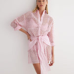"Front view of the Jesabel Pink Dress, showing its mini shirt dress design with square patterned Broderie Anglaise cotton, button fastening, pointed collar, and waist-cinching tie."