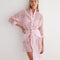 "Front view of the Jesabel Pink Dress, showing its mini shirt dress design with square patterned Broderie Anglaise cotton, button fastening, pointed collar, and waist-cinching tie."