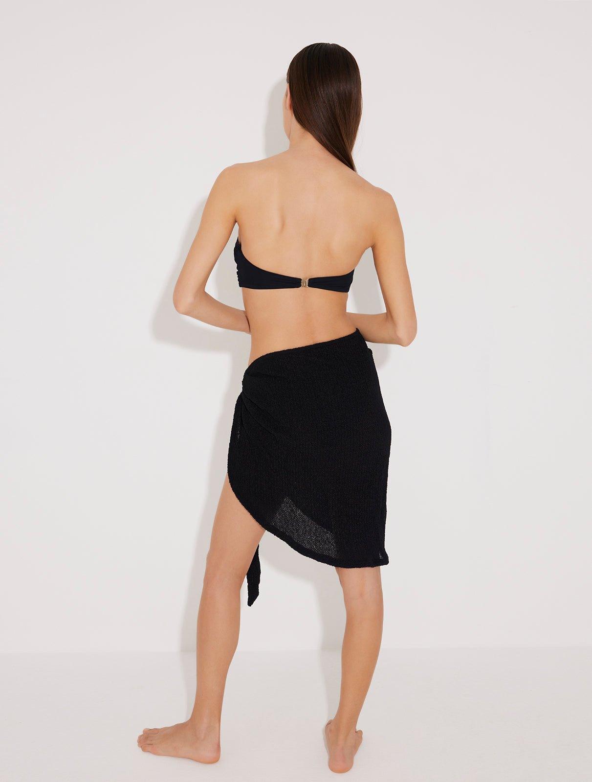 "Back view of a model in a black sarong with a gold accessory, highlighting the sarong's sleek design and secure fit."