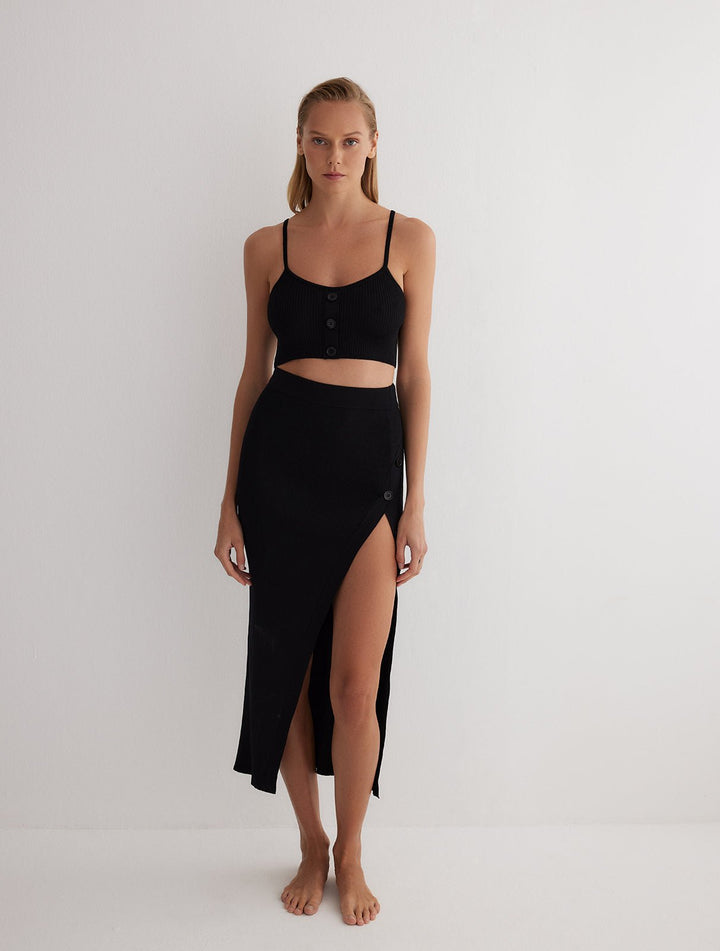Front View: Model in Jules Black Skirt - MOEVA Luxury Swimwear, Knitted Skirt, Button Detail Throughout, Side Assymmetrical Skirt, Elasticated Waistband, Front Slit, MOEVA Luxury Swimwear