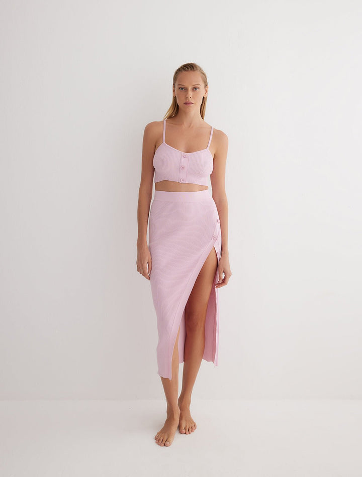 Front View: Model in Jules Pink Skirt - MOEVA Luxury Swimwear, Knitted Skirt, Button Detail Throughout, Side Assymmetrical Skirt, Elasticated Waistband, Front Slit, MOEVA Luxury Swimwear