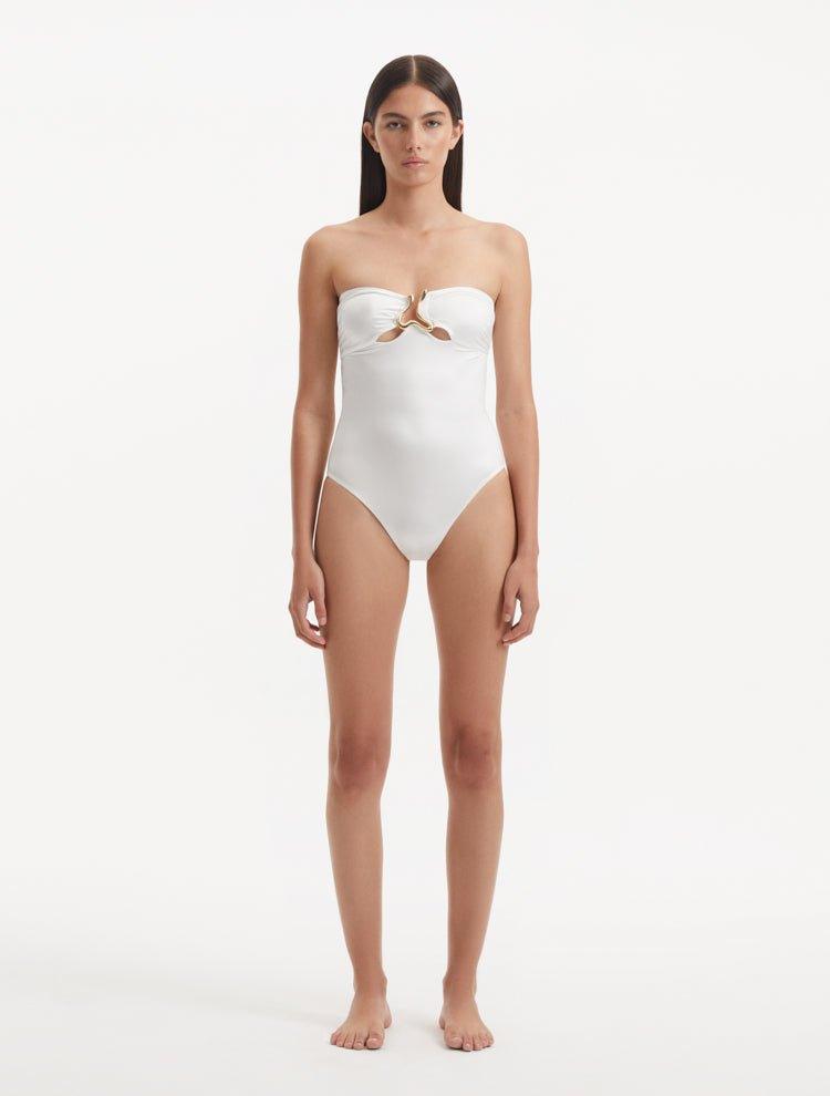 Model showcasing the Kenna White Swimsuit with its elegant strapless neckline and gold sculpted accessory detail.