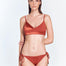 "Model wearing Maelys Red Ochre Bikini Bottom from the front view, showing low-rise waist, satin and matte contrast panels, and side ties with gold-plated stoppers."