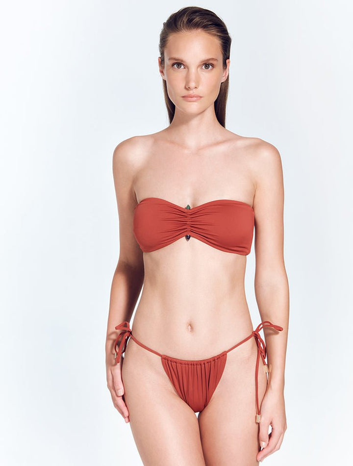 Front View: Model in Maissa Red Ochre Bikini Bottom - MOEVA Luxury Swimwear, Brazilian Bottom, Low Rise, Straps Ties at the Side, Comfort, Soft Touch Fabric MOEVA Luxury Swimwear