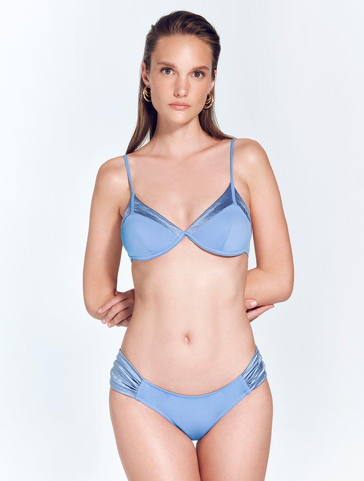 "Model wearing the Manon Blue Bikini Bottom from the front, showing the low-rise waist, small coverage, and ruched satin side straps."