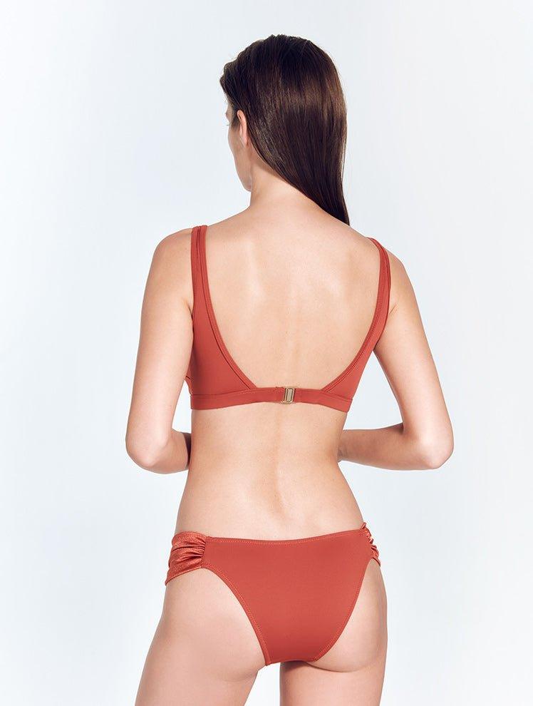 "Back view of a model wearing the Manon Red Ochre Bikini Bottom, featuring ruched satin side straps and a low-rise waist."