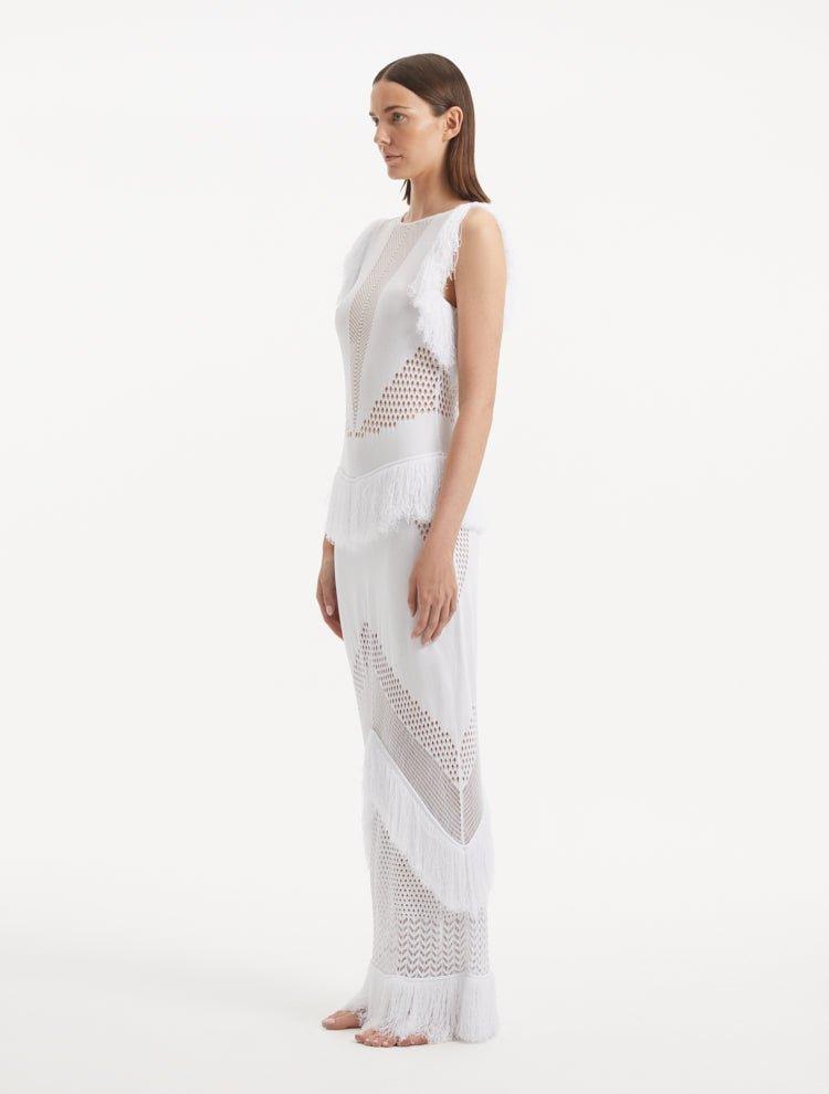 "Side view of the Maris White Dress, emphasizing the close-fitting silhouette, fringe details at the hem, and the gentle contour of the dress as it moves."