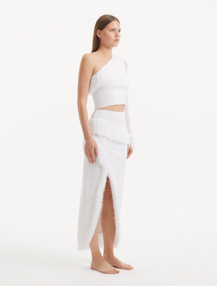 "Model wearing the Monroe White Top and Alani Skirt from the side, emphasizing the one-shoulder cut and the playful movement of the fringes."