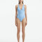 Model showcasing the Naida Baby Blue Swimsuit with a V-neck design and shell-shaped gold buttons, highlighting its elegant and athletic look.