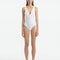 Model wearing the Naida White Swimsuit, showcasing the elegant V-neck design and shell-shaped gold button accents.