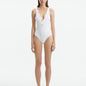 Model wearing the Naida White Swimsuit, showcasing the elegant V-neck design and shell-shaped gold button accents.