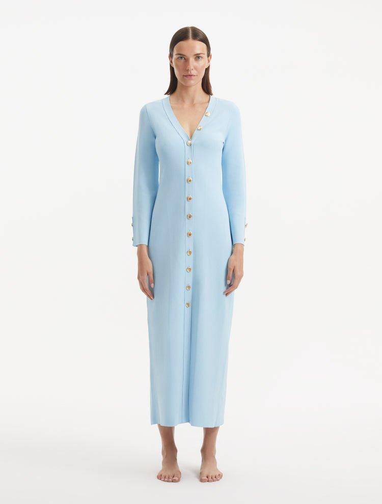 "Model wearing the Nira Baby Blue Dress from the front, highlighting the elegant V-neckline, unique shell-shaped gold buttons, and the luxurious knit fabric. "