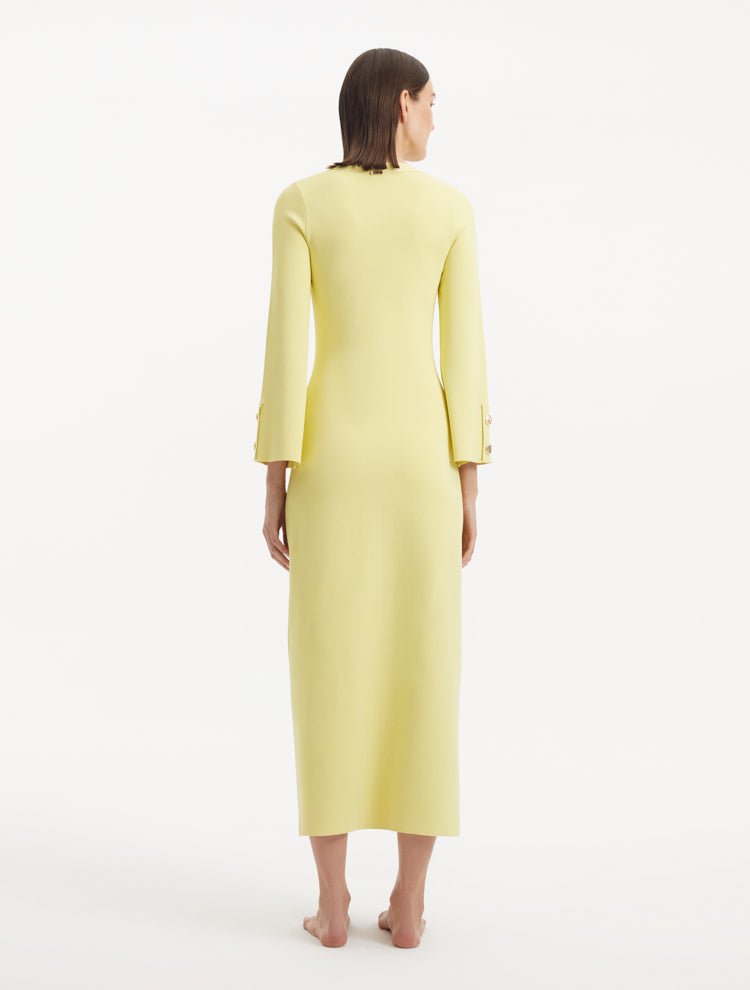 "Model showcasing the Nira Yellow Dress from the back, emphasizing the flowing, ankle-length design and the bright yellow hue. "