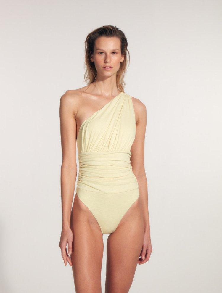 "Model wearing the Penny Yellow Swimsuit from the front, highlighting its one-shoulder design and flattering ruching details on the cups and waist for a cinched-in hourglass silhouette."