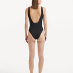  Back view of the Reva Black Swimsuit, emphasizing the sleek low back design and shell-shaped gold buttons.
