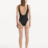  Back view of the Reva Black Swimsuit, emphasizing the sleek low back design and shell-shaped gold buttons.