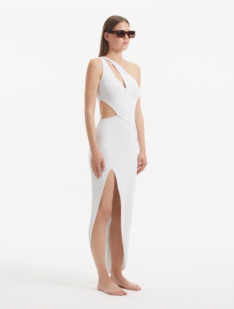 "Model presenting the Shore White Dress from the side, focusing on the enchanting side slit and the ankle-length silhouette. The asymmetric design and ribbed detailing are also featured."