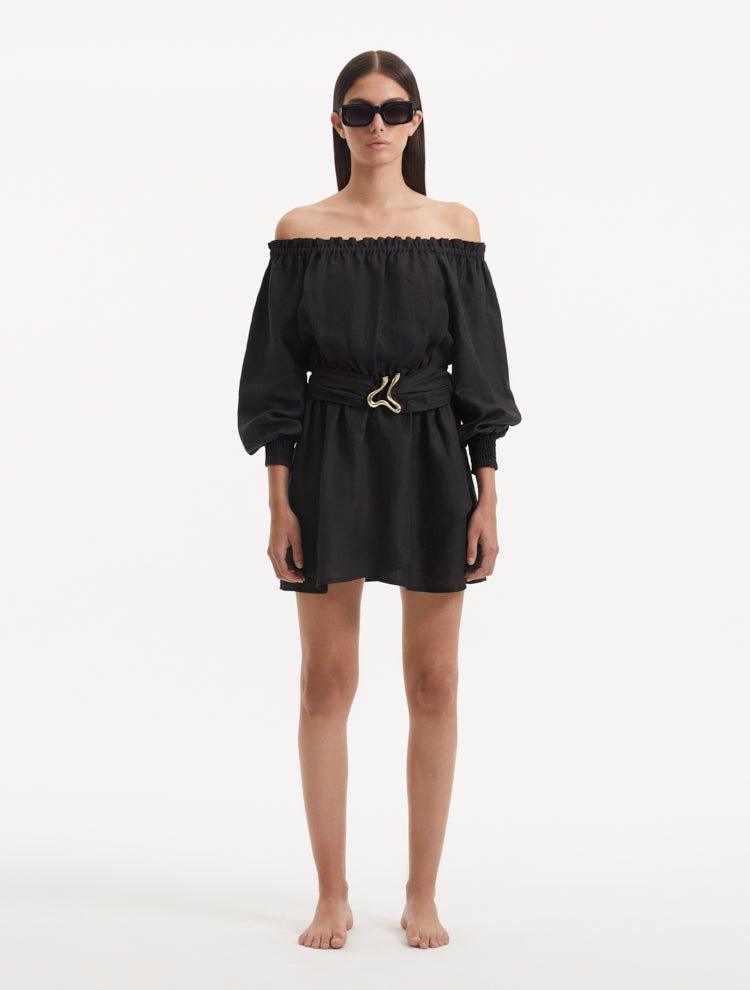 "Model displaying the Sumner Black Dress from the front, emphasizing the ruched neckline, elastic off-the-shoulder design, and long puffed sleeves. "